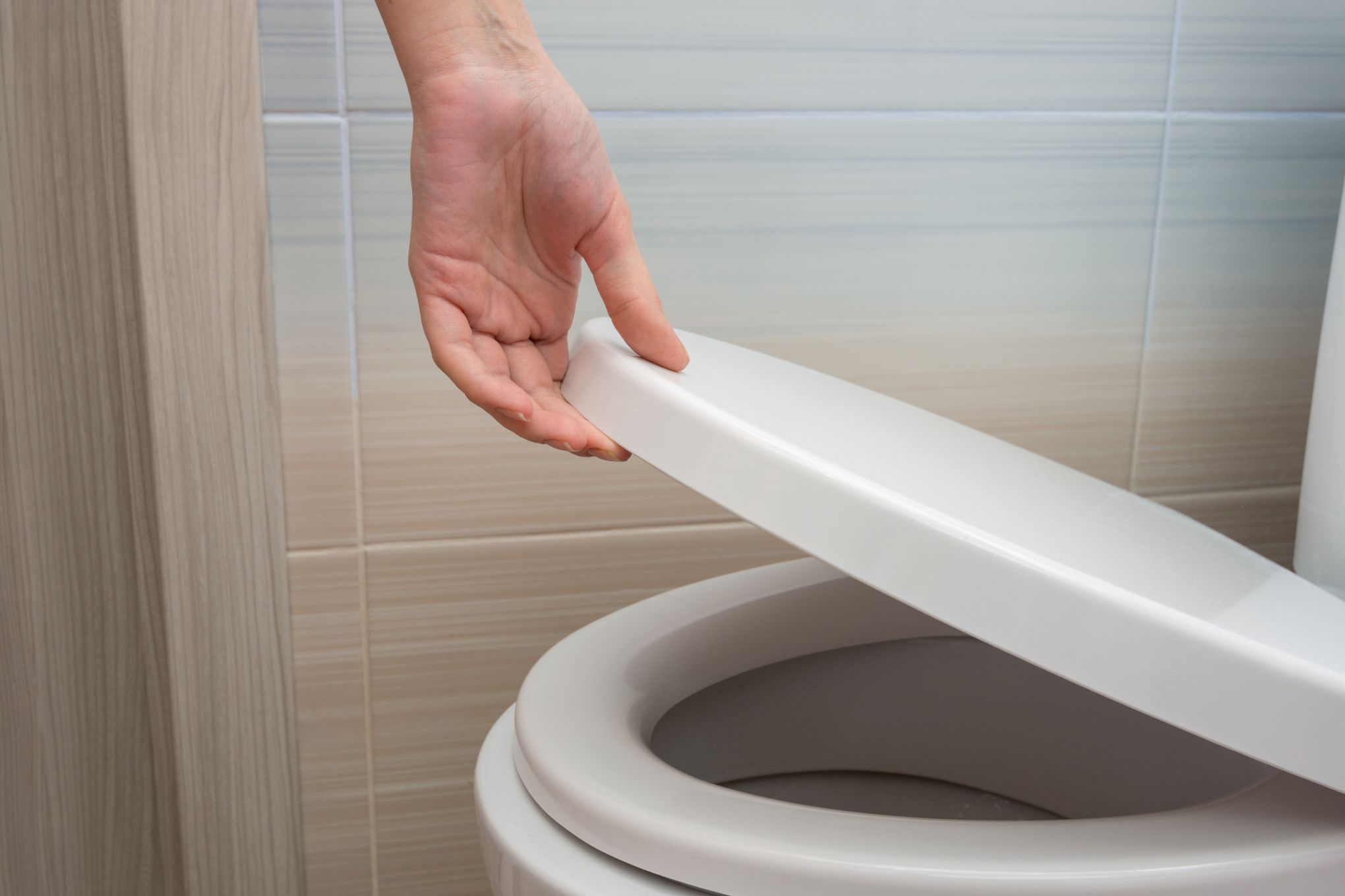 Henkilö avaamassa wc-istuimen kantta.
